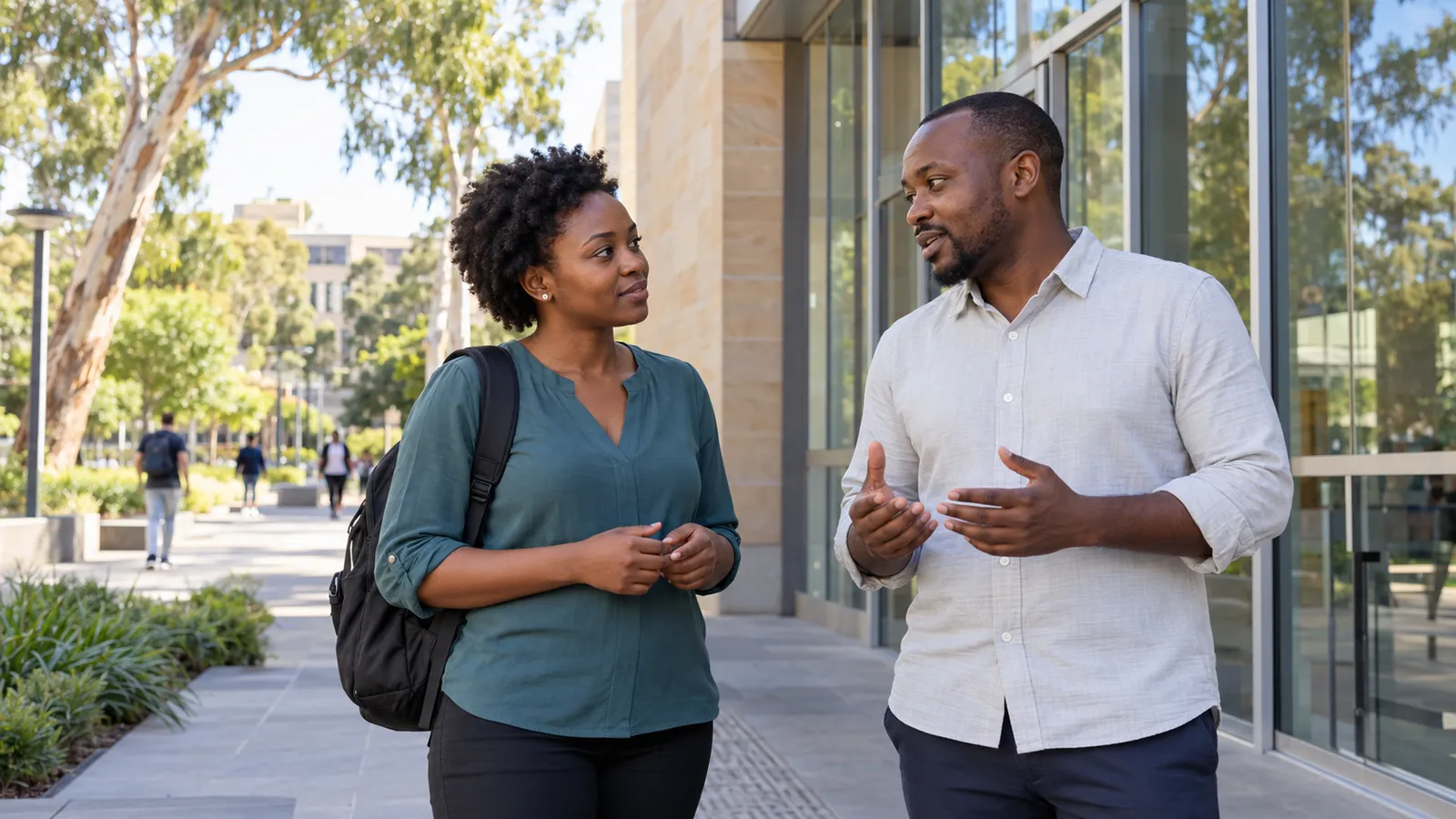 Two Kenyan students talk outside a glass-fronted university building on a sunny Australian campus.